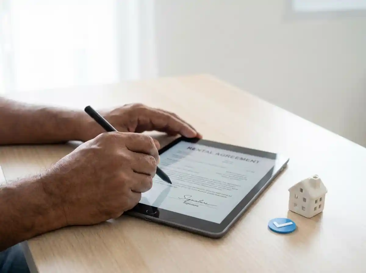 Digital rental agreement being signed on a tablet for NRI property in India with house model on desk